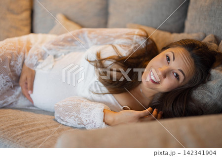 Happy pregnant woman relaxing on couch in a cozy and serene atmosphere Happy pregnant woman relaxing on couch in a cozy and serene atmosphere 142341904