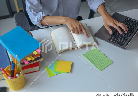 A young male tutor teacher explains a lesson during a virtual class with laptop and books on the table. 142343299