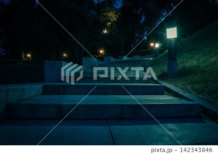 The tiled stairs in the night green park with lanterns in summer. Benches in the park during the summer season at night. Illumination of a park road with lanterns. Park of Eternal Glory. Ukraine The tiled stairs in the night green park with lanterns in summer. Benches in the park during the summer season at night. Illumination of a park road with lanterns. Park of Eternal Glory. Ukraine 142343846