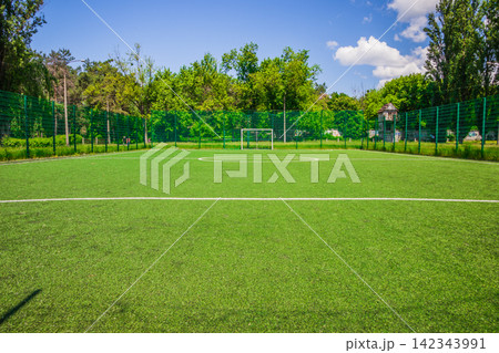 Soccer field with artificial green grass near the school. Amateur football field. Sunny summer day Soccer field with artificial green grass near the school. Amateur football field. Sunny summer day 142343991