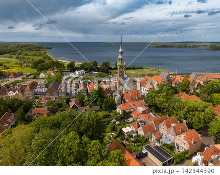 High angle wide horizontal aerial drone photograph of Veere City Hall tower, orange roofs, Lake Veere, coastline, and dramatic storm sky in Veere, Zeeland, Netherlands on sunny summer day 142344390