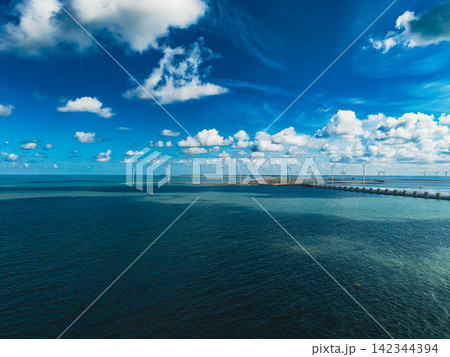 High angle wide horizontal aerial drone photograph of Eastern Scheldt storm surge barrier, wind turbines, sea water, and cloudy blue sky at Neeltje Jans, Zeeland, Netherlands on sunny summer day 142344394