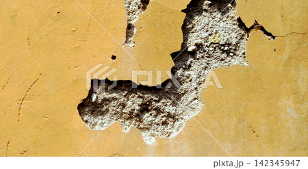 Cracked yellow stucco wall with a damaged plaster texture. Cracked yellow stucco wall with a damaged plaster texture. 142345947