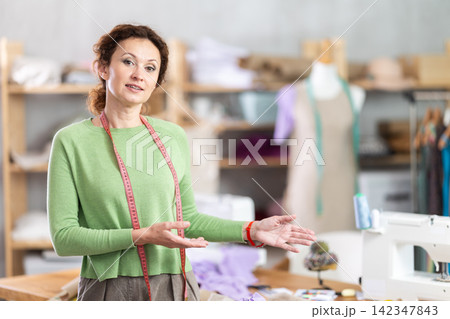 Female tailor welcoming clients into sewing studio Female tailor welcoming clients into sewing studio 142347843
