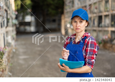 Female cemetery employee stands with report and writes down information. 142348041