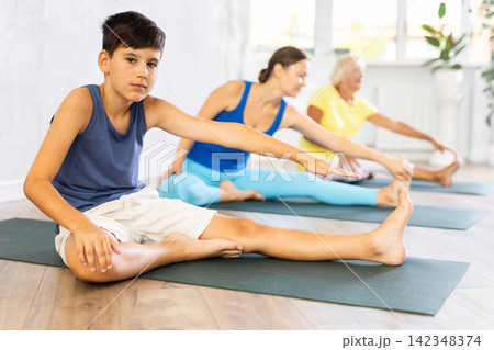 Preteen boy practicing head to knee pose of yoga in light fitness room Preteen boy practicing head to knee pose of yoga in light fitness room 142348374