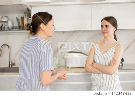 Kind middle-aged mother talking to young daughter in the kitchen Kind middle-aged mother talking to young daughter in the kitchen 142348412