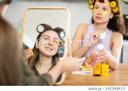 Women in colorful curlers applying eye patches and sharing beauty secrets Women in colorful curlers applying eye patches and sharing beauty secrets 142348413