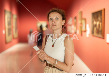 Thoughtful attentive woman standing in front of painting in art museum Thoughtful attentive woman standing in front of painting in art museum 142348641
