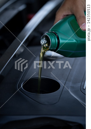 Person pouring fresh motor oil into a car engine during vehicle maintenance. Routine lubrication service performed in a workshop to protect engine components, reduce friction and support reliability. 142350513