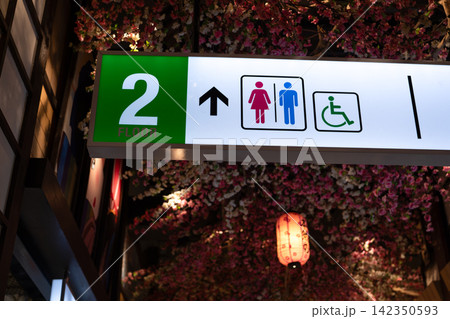 Restroom and accessibility direction sign on the second floor of shopping mall, guiding visitors to male, female and wheelchair friendly facilities indoors. Restroom wayfinding sign. Public toilet. Restroom and accessibility direction sign on the second floor of shopping mall, guiding visitors to male, female and wheelchair friendly facilities indoors. Restroom wayfinding sign. Public toilet. 142350593