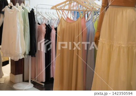 Sustainable fashion display with pastel women dresses hanging on wooden hangers inside clothing boutique. Eco conscious shopping, slow fashion and responsible retail choices. Ethical retail culture. 142350594