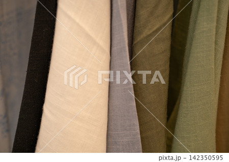 Close up of neutral fabric swatches hanging in fashion studio. Natural textile texture. Sustainable clothing design, ethical sourcing and conscious material selection. Sustainable fashion materials. Close up of neutral fabric swatches hanging in fashion studio. Natural textile texture. Sustainable clothing design, ethical sourcing and conscious material selection. Sustainable fashion materials. 142350595