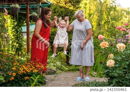Mother And Grandmother Lifting Happy Girl In Flower Garden Mother And Grandmother Lifting Happy Girl In Flower Garden 142350961