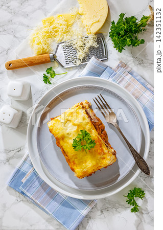 Lasagne mit Hackfleisch prepared in popular German style with layered ground beef and melted cheese served on a grey plate on a marble background, vertical, not AI 142351132