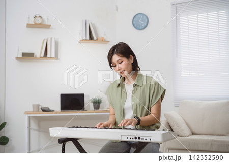Young woman playing electronic keyboard in modern living room during daytime, relaxed home atmosphere, casual fashion Young woman playing electronic keyboard in modern living room during daytime, relaxed home atmosphere, casual fashion 142352590