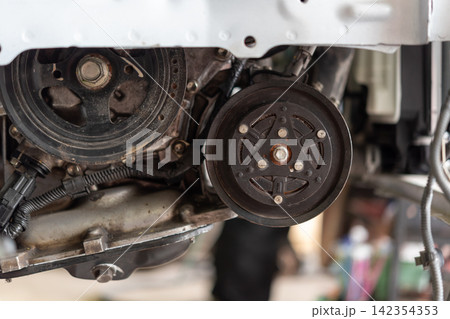 Closeup of automotive engine pulley compressor components showing mechanical parts wiring metal assembly during vehicle maintenance repair Closeup of automotive engine pulley compressor components showing mechanical parts wiring metal assembly during vehicle maintenance repair 142354353