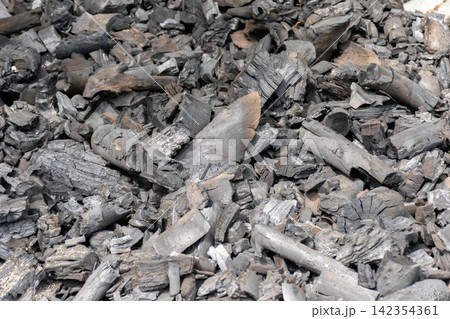 Pile of burned hardwood charcoal pieces showing black gray textures irregular shapes suitable for fuel barbecue cooking traditional charcoal production 142354361