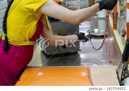 Confectioner Feeding Striped Sugar Rope into Hard Candy Sizing Machine Confectioner Feeding Striped Sugar Rope into Hard Candy Sizing Machine 142354852