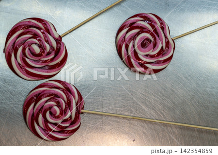 Three Round Swirl Lollipops with Wooden Sticks on Stainless Steel Counter Top 142354859