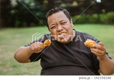 Portrait of fat man biting and stuffing fried chicken into his mouth Portrait of fat man biting and stuffing fried chicken into his mouth 142356280