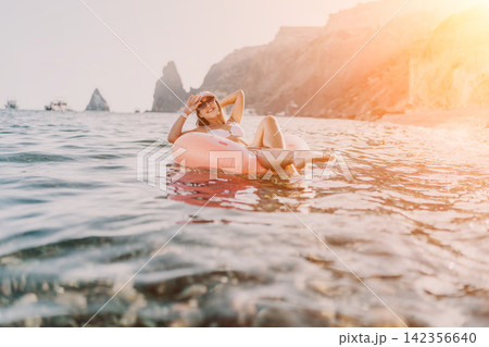 Woman, floating, sea. Young woman enjoying summer vacation, relaxing on inflatable ring near rocky coast. Woman, floating, sea. Young woman enjoying summer vacation, relaxing on inflatable ring near rocky coast. 142356640