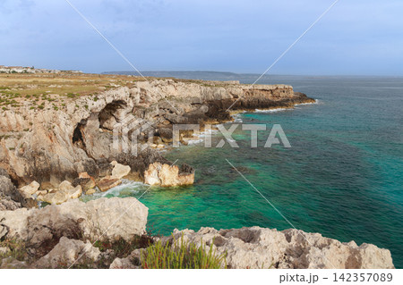 Rugged coastal cliffs meet turquoise sea waters under a vast sky Rugged coastal cliffs meet turquoise sea waters under a vast sky 142357089