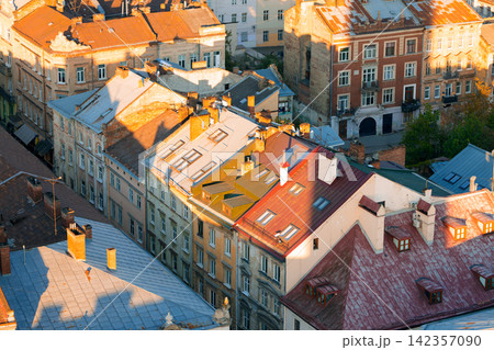 Golden hour sunlight illuminates aged rooftops of historic European city buildings Golden hour sunlight illuminates aged rooftops of historic European city buildings 142357090