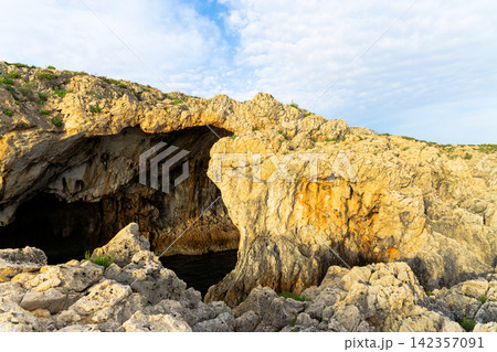 Natural rock archway carved by the sea, revealing a dark cave entrance Natural rock archway carved by the sea, revealing a dark cave entrance 142357091