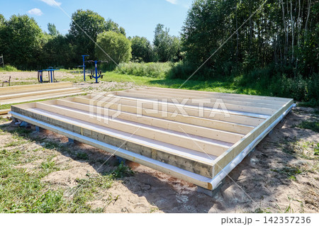 Timber floor frame assembled on concrete blocks with parallel wooden joists forming base for future building construction. 142357236