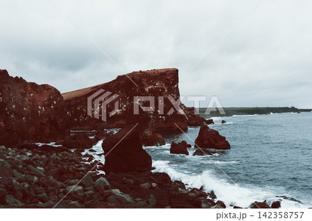 Karlinn sea stack beyond rust-red cliffs in muted vintage film color, Valahnukamol, Iceland 142358757