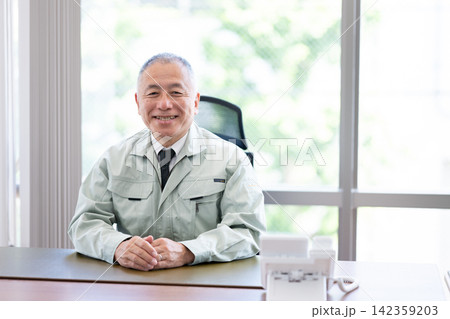 デスクで微笑む作業着姿の中高年男性経営者 デスクで微笑む作業着姿の中高年男性経営者 142359203