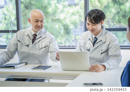 ミーティング　作業着で会話するベテランと若手 142359455