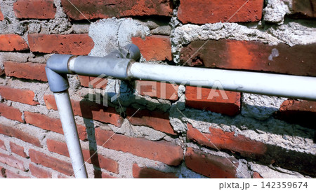 Horizontal PVC water pipe on a rough red brick wall. 142359674
