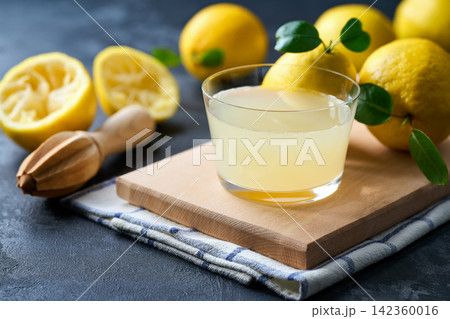 Organic lemon juice in a glass on table. Freshly squeezed lemon juice in a glass with halved lemons on dark table, selective focus. 142360016