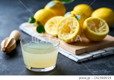 Organic lemon juice in a glass on table. Freshly squeezed lemon juice in a glass with halved lemons on dark table, selective focus. 142360019