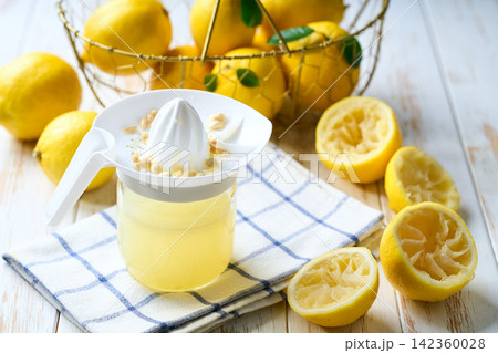 Fresh lemon juice in bowl and ripe lemons on white table, selective focus. freshly squeezed lemon juice . 142360028