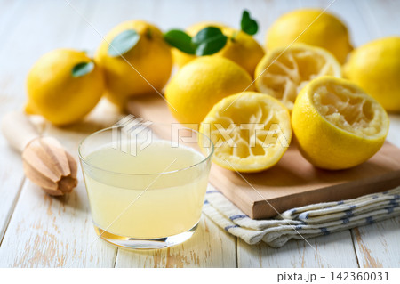 homemade lemon juice in a glass on table. Freshly squeezed lemon juice in a glass with halved lemons on white table, selective focus. 142360031