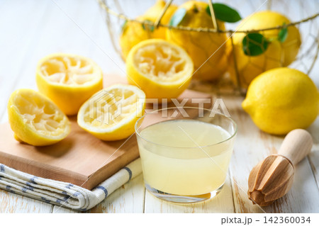 homemade lemon juice in a glass on table. Freshly squeezed lemon juice in a glass with halved lemons on white table, selective focus. 142360034