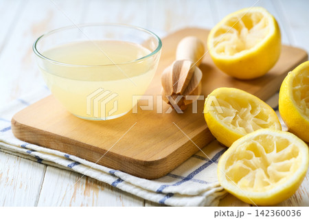 Freshly squeezed lemon juice in a bowl with halved lemons on white table, selective focus. Organic lemon juice in a bowl on table. 142360036