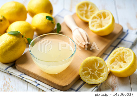 Bowl with fresh lemon juice, squeezer and ripe lemons on white table, close up. Homemade lemon juice in a bowl on table. 142360037