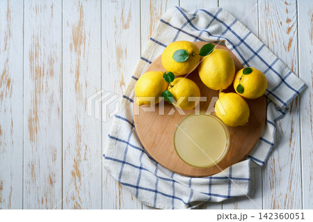 homemade lemon juice in glass and ripe lemons on white wooden table, with copy space for text. Top vie 142360051