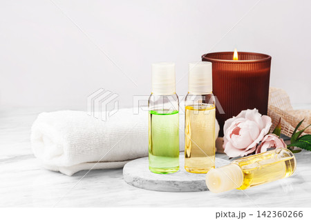 Cosmetic beauty bottles with burning aroma candle, towel and pink roses on marble table, spa and wellness background Cosmetic beauty bottles with burning aroma candle, towel and pink roses on marble table, spa and wellness background 142360266