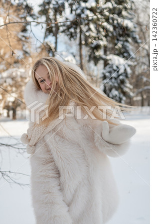 Happy young woman in white fur coat enjoying snowy winter day 142360722