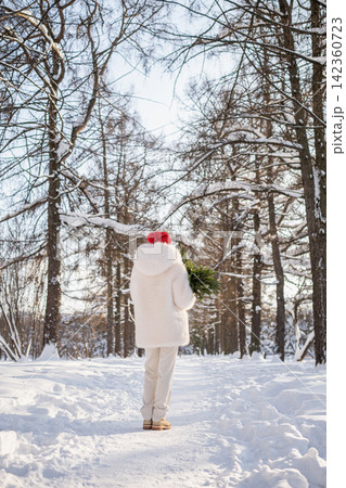 Woman carrying Christmas tree through snowy winter forest 142360723