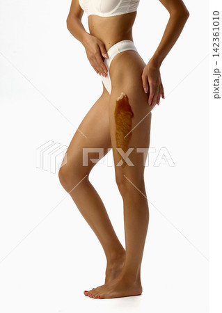 Standing woman showing wax strip to upper thigh. Standing woman showing wax strip to upper thigh. 142361010