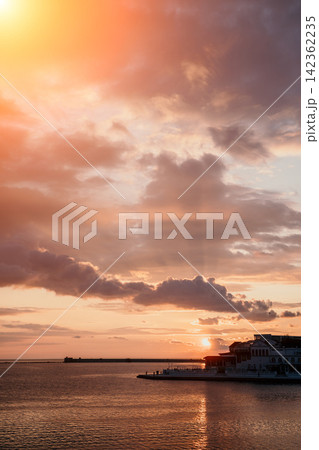 Sunset clouds harbor featuring dramatic orange light over a quiet coastal resort area during a peaceful twilight evening Sunset clouds harbor featuring dramatic orange light over a quiet coastal resort area during a peaceful twilight evening 142362235