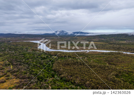 Aerial view of the Lake Arragan estuary surrounded by native coastal vegetation and natural landscape beneath a cloudy sky within Yuraygir National Park on the NSW North Coast, Australia. Aerial view of the Lake Arragan estuary surrounded by native coastal vegetation and natural landscape beneath a cloudy sky within Yuraygir National Park on the NSW North Coast, Australia. 142363026