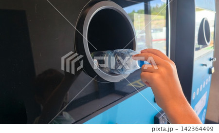Child recycling a plastic bottle at a public recycling machine. Concepts: sustainability, environmental education, circular economy, responsible consumption. 142364499