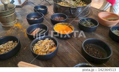 Assorted spices and dried herbs are arranged in bowls on a rustic wooden worktable during traditional food preparation. Concepts: culinary craftsmanship, natural ingredients, cultural tradition. Assorted spices and dried herbs are arranged in bowls on a rustic wooden worktable during traditional food preparation. Concepts: culinary craftsmanship, natural ingredients, cultural tradition. 142364513